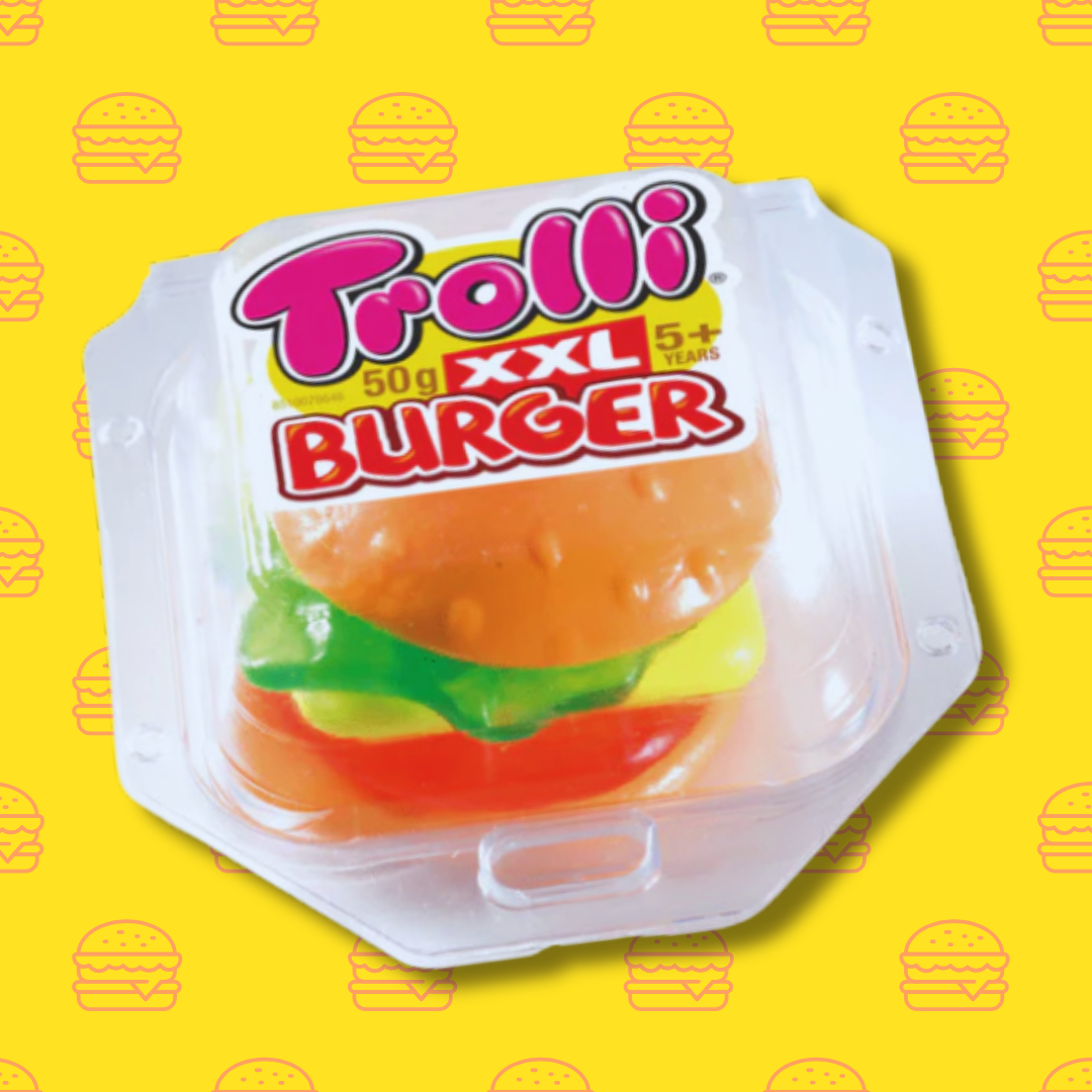 Image d'une boîte contenant une version XXL du mini burger. La boîte est posée sur un fond jaune avec un ensemble de petits burgers. Sur celle-ci on retrouve la marque 'Trolli' écrit en gros et en rose. L'énorme bonbon en forme de Hamburger  à l'intérieur est composé de plusieurs tranches de bonbon gélifié. 