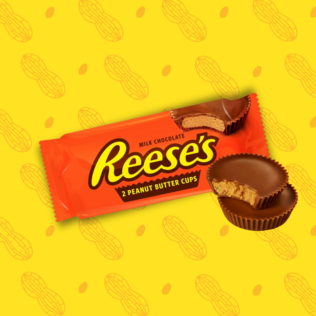 Sur cette image apparaît l'emblématique snack sucré salé américain. Les Reese's Cups sont conditionnées dans un emballage rectangulaire de couleur orange. Deux cups de Reese's sont placées devant l'emballage, ces gourmandises sont rondes et fourrées à la cacahuète. 